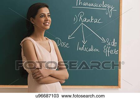 Thoughtful female teacher standing against green board View Large Photo Image Stock Image - Thoughtful female teacher standing against green board . Fotosearch