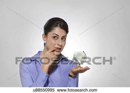 Thoughtful Indian businesswoman holding globe over gray background View Large Photo Image Stock Photography - Thoughtful Indian businesswoman holding globe over gray background. Fotosearch