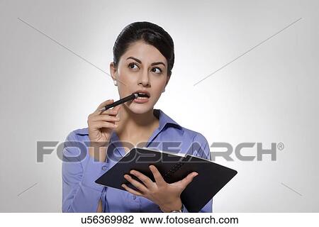 Stock Image - Thoughtful Indian businesswoman with notebook and pen against gray background. Fotosearch
