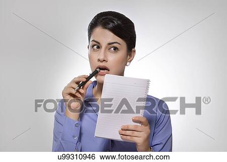Stock Photograph - Thoughtful Indian businesswoman with notebook and pen over gray background. Fotosearch
