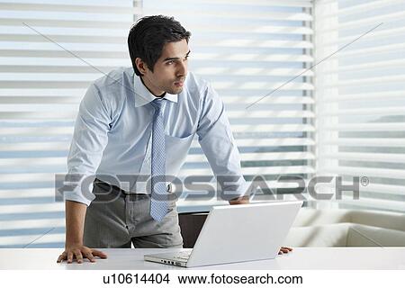 Thoughtful young business man standing at his desk View Large Photo Image Picture - Thoughtful young business man standing at his desk . Fotosearch