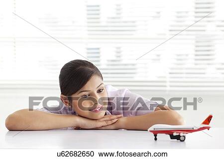 Stock Image - Thoughtful young business woman looking at airplane model . Fotosearch