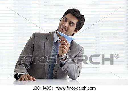 Thoughtful young businessman holding paper plane at his desk View Large Photo Image Stock Image - Thoughtful young businessman holding paper plane at his desk . Fotosearch