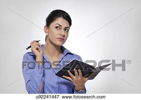 Thoughtful young businesswoman holding note pad and pen against gray background View Large Photo Image Stock Photo - Thoughtful young businesswoman holding note pad and pen against gray background. Fotosearch