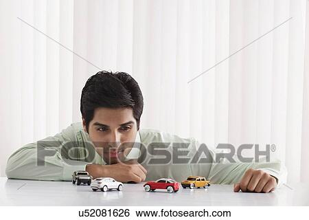 Thoughtful young male executive looking at model cars View Large Photo Image Stock Photograph - Thoughtful young male executive looking at model cars . Fotosearch