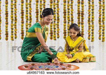Stock Image - Woman arranging diyas on a rangoli . Fotosearch