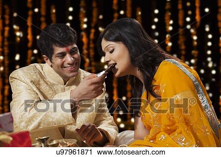 Stock Image - Woman eating chocolate offered by her brother. Fotosearch