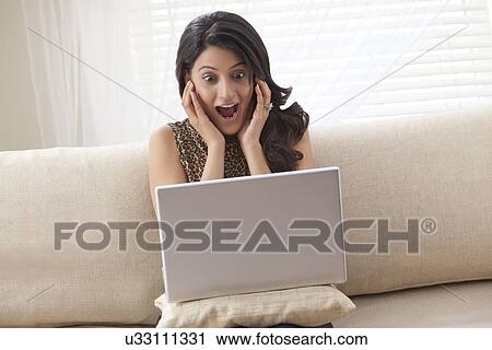 Stock Image - Woman getting a shock after looking at laptop. Fotosearch