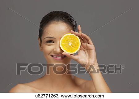 Stock Image - Woman holding an orange slice over her eye . Fotosearch