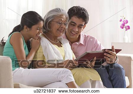Stock Photo - Woman looking at photo album with grandchildren. Fotosearch