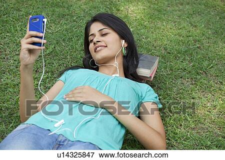 Woman lying on grass listening to mp3 player View Large Photo Image Stock Photo - Woman lying on grass listening to mp3 player . Fotosearch