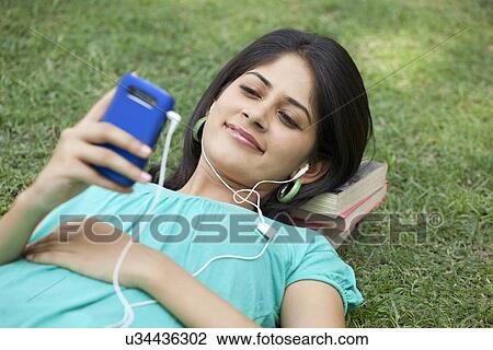 Stock Image - Woman lying on grass listening to music . Fotosearch