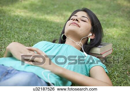 Woman lying on grass listening to music with eyes closed View Large Photo Image Stock Photograph - Woman lying on grass listening to music with eyes closed . Fotosearch