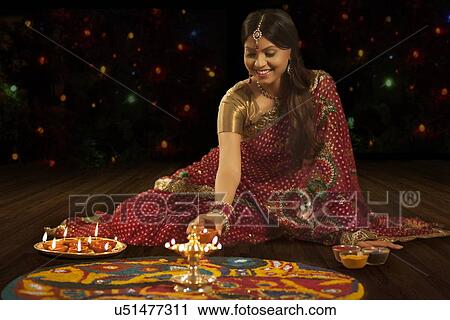 Stock Image - Woman placing a diya on a rangoli. Fotosearch