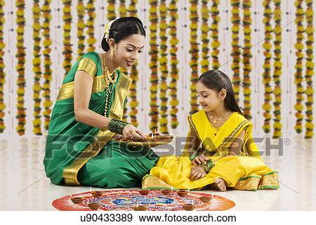 Stock Photo - Woman placing diyas on a rangoli . Fotosearch