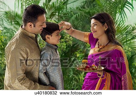 Stock Image - Woman putting tikka on her sons forehead . Fotosearch