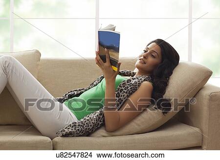 Picture - Woman reading a book on a sofa. Fotosearch