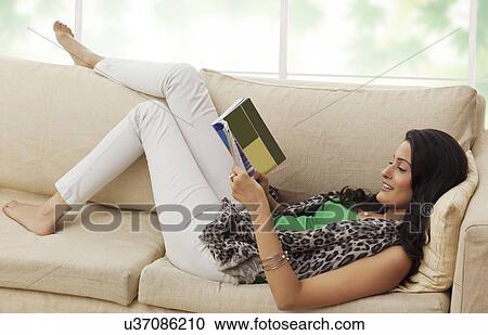 Stock Image - Woman reading a book on a sofa. Fotosearch