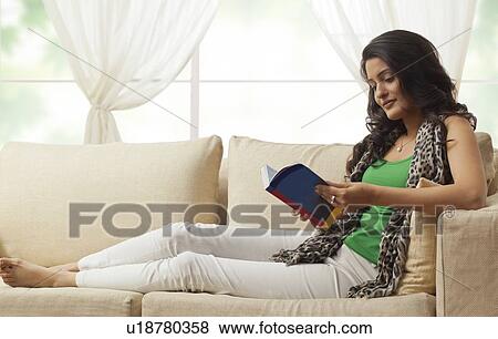 Stock Photo - Woman reading a book on a sofa. Fotosearch
