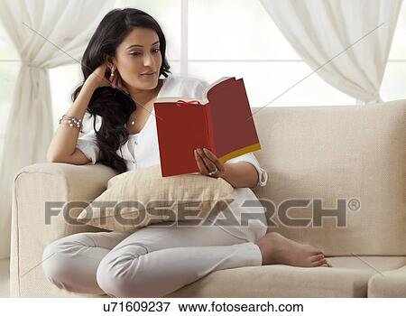 Woman reading a book on a sofa View Large Photo Image Stock Photo - Woman reading a book on a sofa. Fotosearch