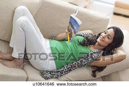 Woman reading a book on a sofa View Large Photo Image Stock Photograph - Woman reading a book on a sofa. Fotosearch
