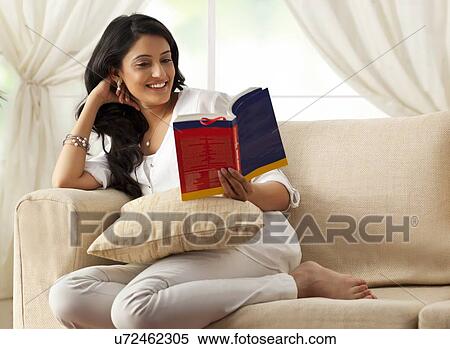 Stock Photography - Woman reading a book on a sofa. Fotosearch