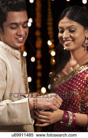 Stock Photography - Woman tying rakhi on her brother's hand. Fotosearch