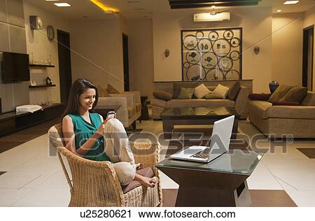 Woman using cell phone while sitting on wicker chair in front of coffee table with laptop at home View Large Photo Image Stock Image - Woman using cell phone while sitting on wicker chair in front of coffee table with laptop at home . Fotosearch