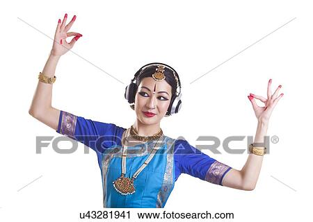 Stock Image - Woman wearing headphone while performing Bharatanatyam over white background. Fotosearch