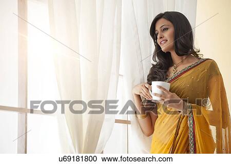 Stock Image - Woman with a mug of tea looking out a window. Fotosearch
