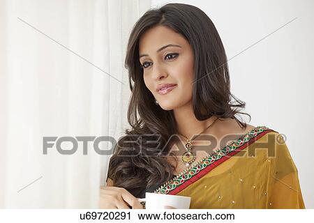 Stock Image - Woman with a mug of tea looking out a window. Fotosearch