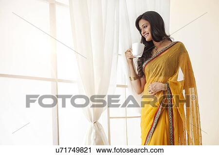 Stock Image - Woman with a mug of tea looking out a window. Fotosearch
