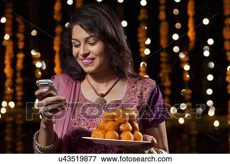 Stock Photo - Woman with a plate of sweets reading an sms. Fotosearch