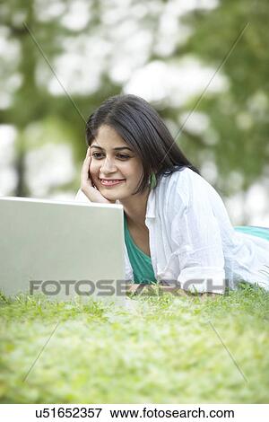 Stock Photo - Woman with hand on chin looking at laptop screen and smiling . Fotosearch