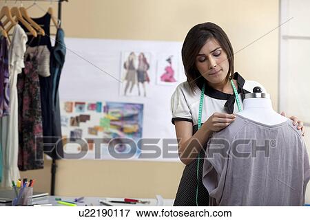 Stock Photo - Young beautiful designer fixing dress on mannequin . Fotosearch