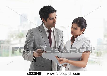 Young businessman looking at female colleague with document in hand View Large Photo Image Stock Image - Young businessman looking at female colleague with document in hand . Fotosearch