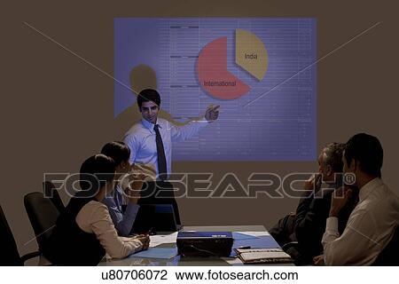 Stock Image - Young businessman presenting on projection screen in meeting . Fotosearch