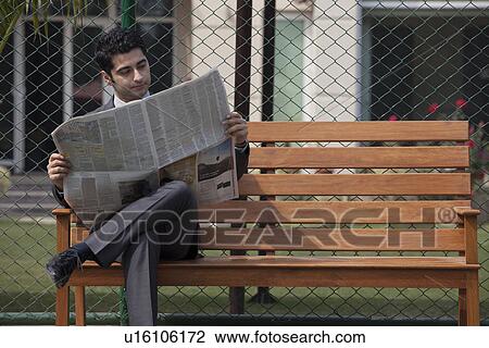 Young businessman reading newspaper while sitting on bench in tennis court View Large Photo Image Stock Image - Young businessman reading newspaper while sitting on bench in tennis court . Fotosearch