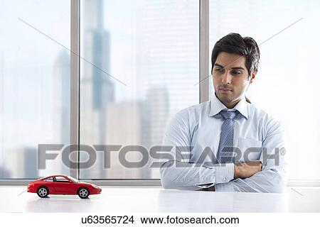 Young businessman with hands folded looking at car model View Large Photo Image Picture - Young businessman with hands folded looking at car model . Fotosearch