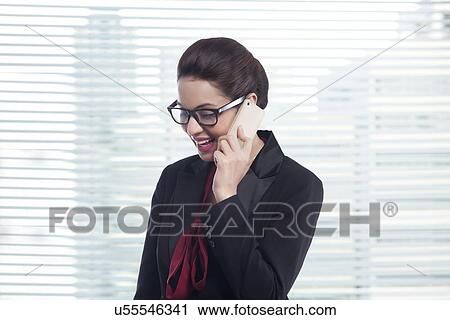 Stock Image - Young businesswoman answering mobile phone in office. Fotosearch