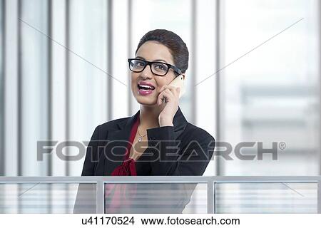 Young businesswoman answering smart phone in office View Large Photo Image Picture - Young businesswoman answering smart phone in office. Fotosearch