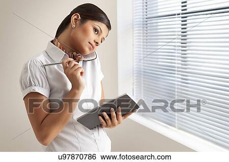Stock Photograph - Young businesswoman busy on phone call with diary at office . Fotosearch