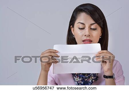 Stock Photo - Young businesswoman holding confidential envelope against gray background. Fotosearch