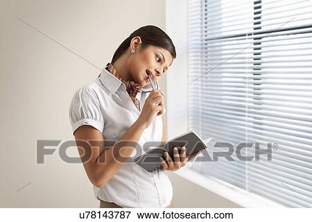 Stock Photo - Young businesswoman on phone call while holding diary at office . Fotosearch