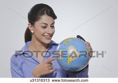 Young businesswoman pointing at globe against gray background View Large Photo Image Stock Image - Young businesswoman pointing at globe against gray background. Fotosearch