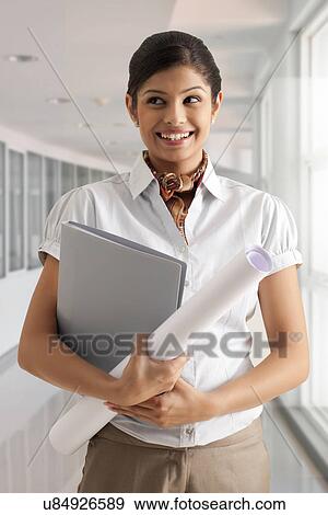 Young businesswoman smiling confidently while holding documents View Large Photo Image Stock Photo - Young businesswoman smiling confidently while holding documents . Fotosearch