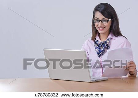 Stock Image - Young businesswoman using laptop at office desk. Fotosearch