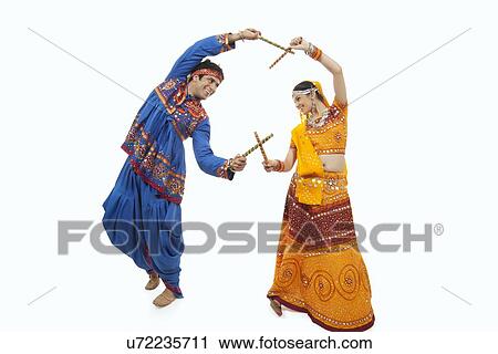 Stock Image - Young couple in traditional wear performing Dandiya Raas over white background. Fotosearch