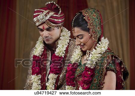 Stock Photo - Young couple wearing garlands looking down . Fotosearch
