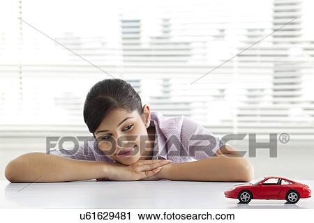 Stock Image - Young female executive dreaming at office white looking at car model . Fotosearch